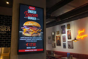 Menu board digitale in una hamburgeria che mostra la promozione di uno smash burger su un monitor professionale verticale.