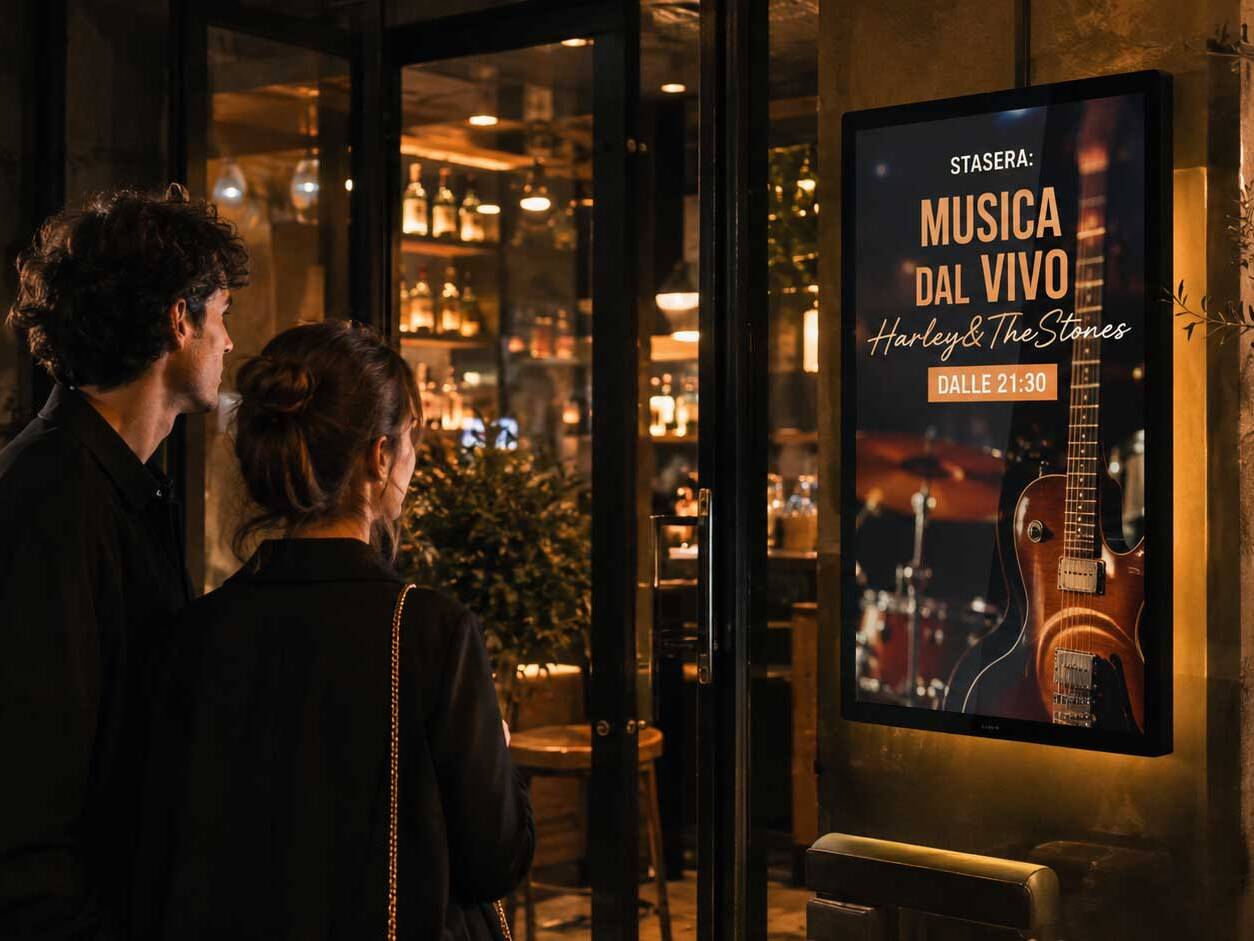 Display digitale all’ingresso di un locale che promuove una serata di musica dal vivo con nome dell’evento e orario.